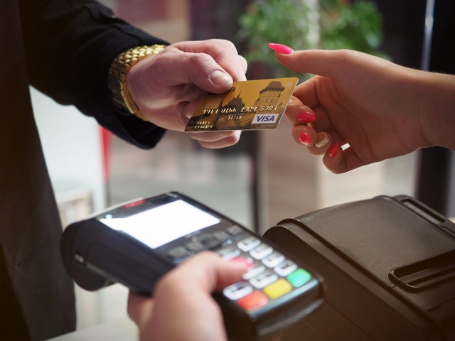 A picture of a man hand handling a via visa debit card to a woman hand holding a swiping machine