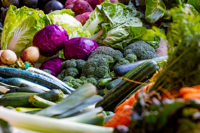 An picture of different vegetables like red and green cabbages, broccoli, white onions, sweet potatoes and cucumbers