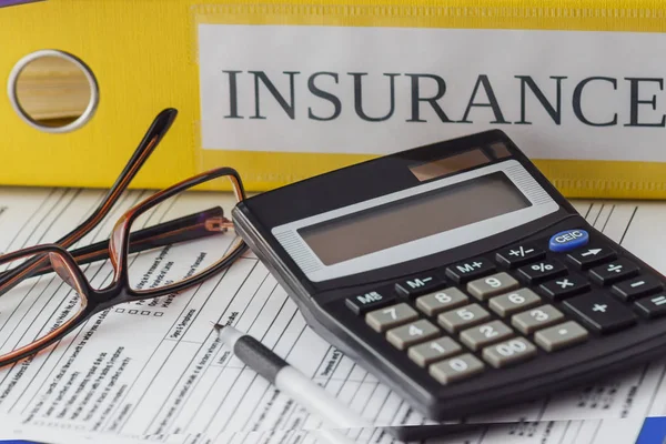 Clean insurance form, folders, glasses, calculator and a pen, soft focus background