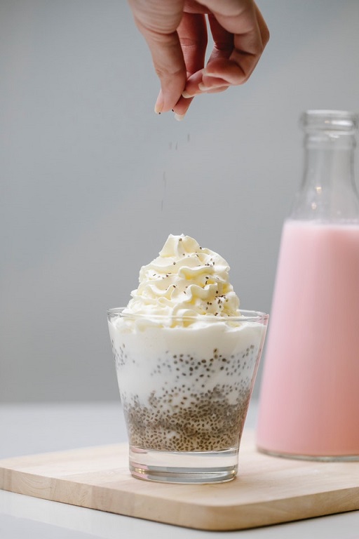 A bottle of yoghurt next to a glass of dressed dessert with cream