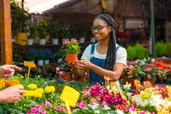 Happy female customer buying flowers from a gardener in a nursery inside the greenhouse