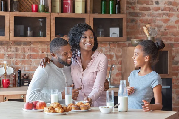 Cheerful african family drinking milk and eating sweets at kitchen,