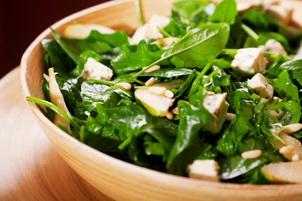 Fresh spinach salad with blue cheese, pears and honey served in a salad bowl, close up