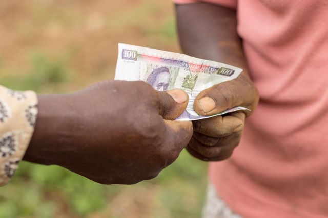 2 farmers exchanging a hundred Kenyan shillings note